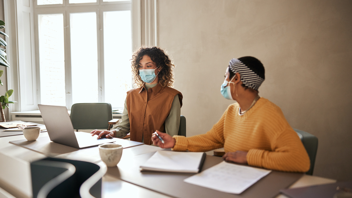 2-women-in-face-masks-work-in-conference-room-leaders-prioritize-well-being-over-leadership